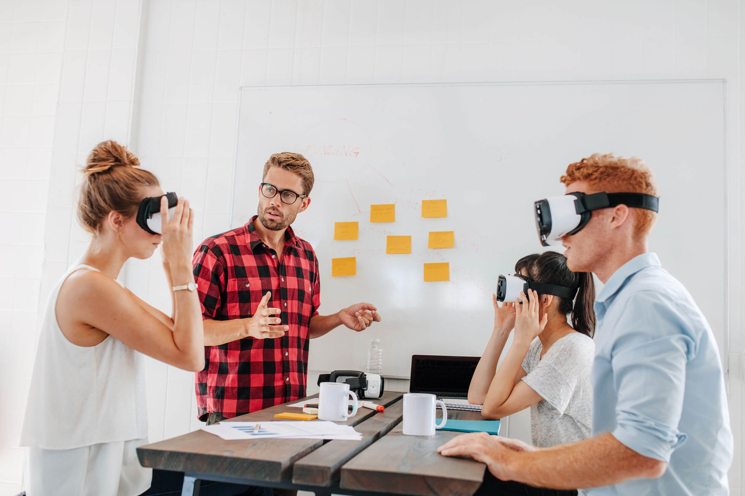 Young men and women sitting at a table with virtual reality goggles. Business team testing virtual reality headset in office meeting.